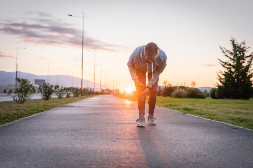 Woman experiencing knee pain during outdoor exercise at sunrise, representing joint discomfort related to arthritis and the importance of exercise.